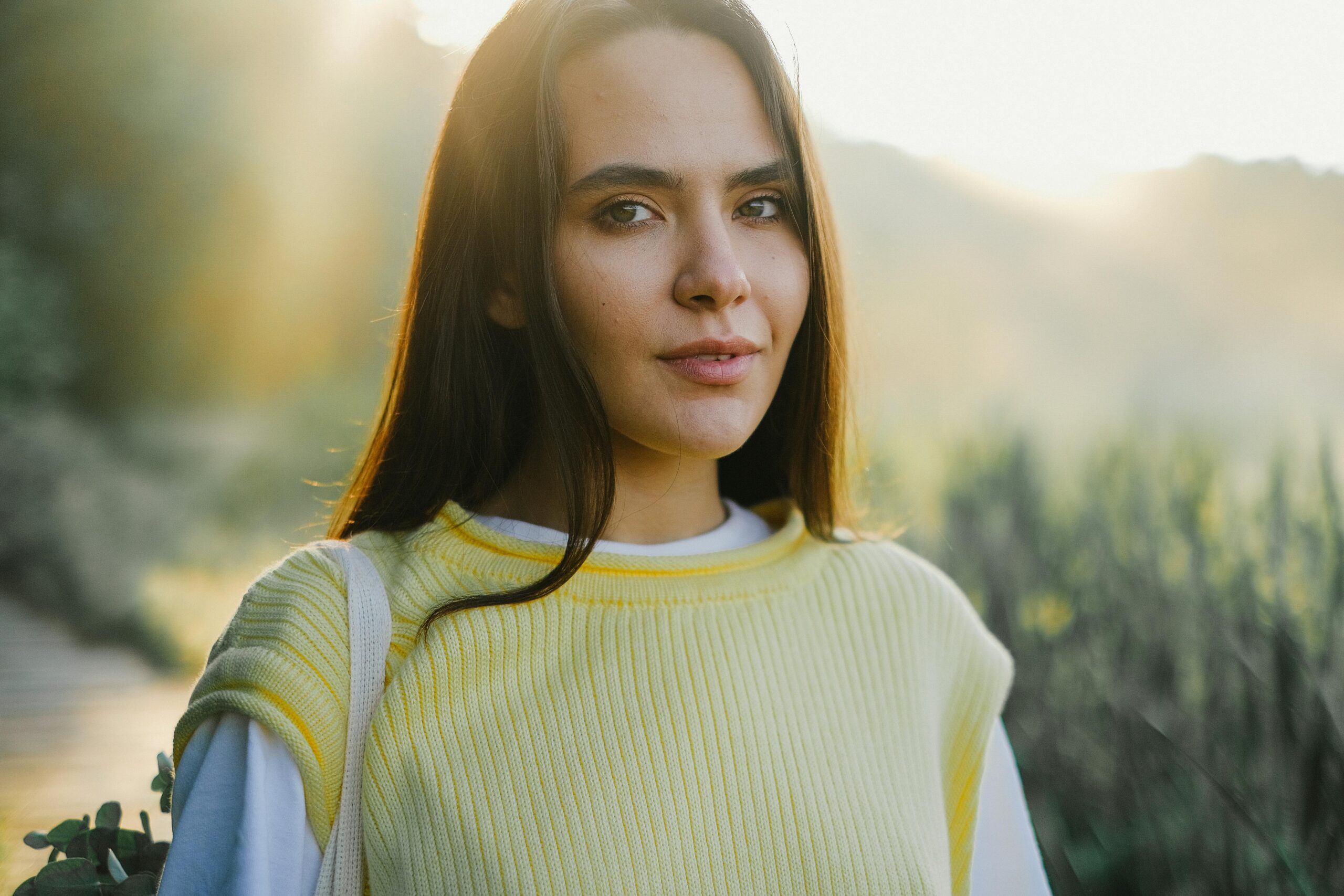 Close-up portrait of a young woman in a yellow knitted vest with natural sunlight outdoors.